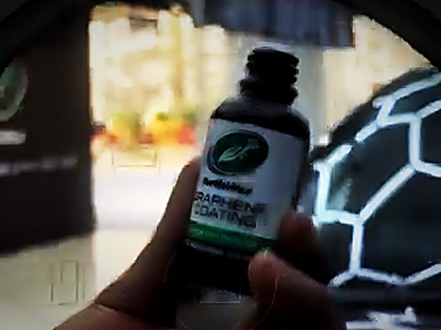 A technician holding a genuine Turtle Wax Graphene Coating bottle and applicator pad inside the Tellapur studio