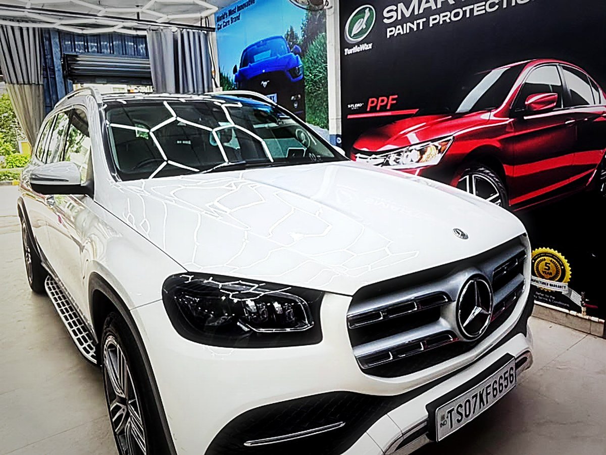 A white Mercedes-Benz GLS beside the Smart Shield paint protection film display at Turtle Wax Studio Tellapur